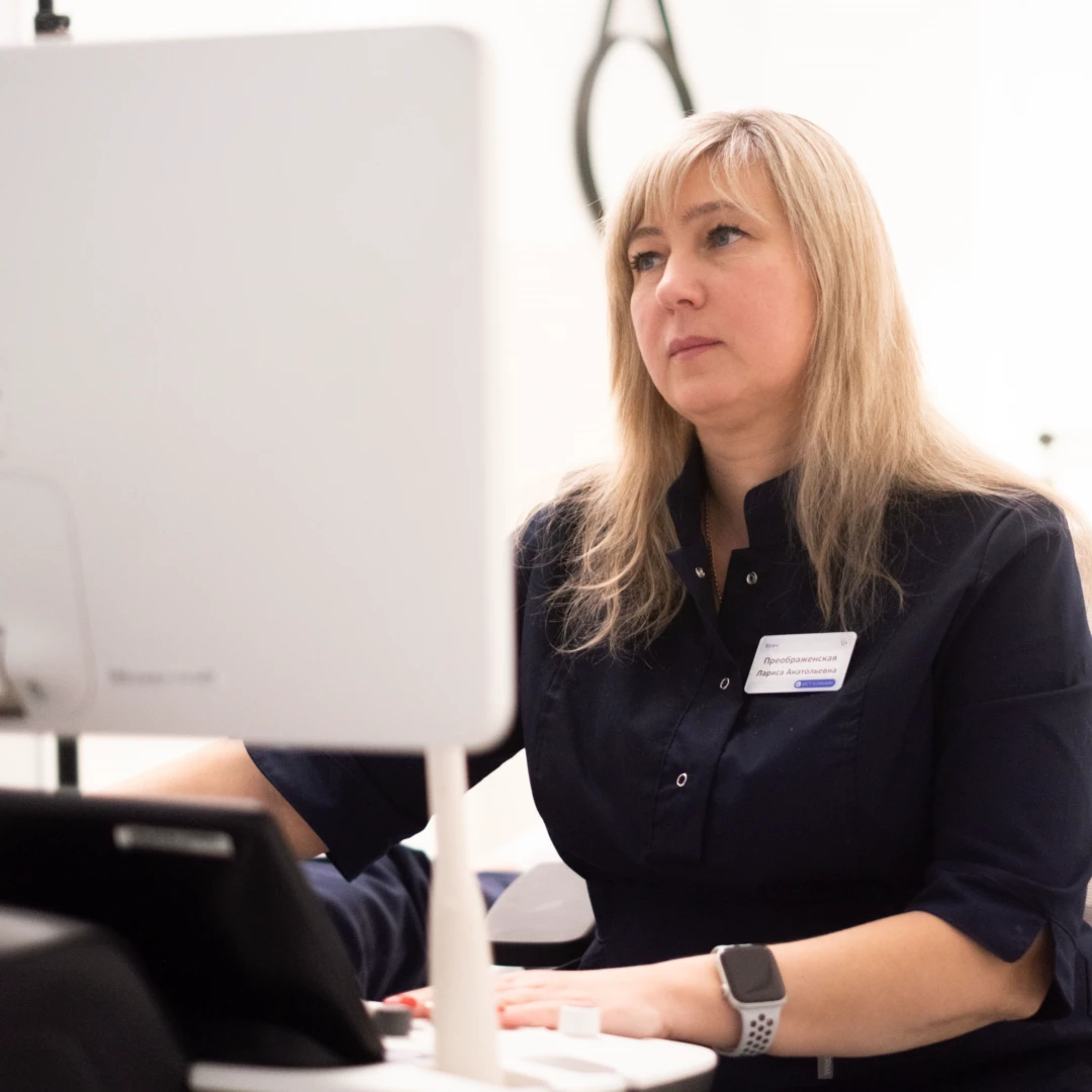 Женщина врач в темно-синем медицинском костюме выполняет УЗИ желчных протоков пациентке.