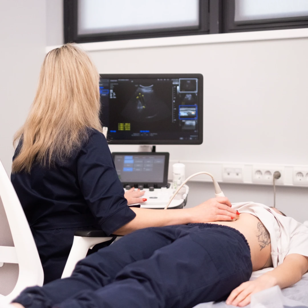 Женщина врач в темно-синем медицинском костюме проводит УЗИ желчных протоков пациентке, лежащей на кушетке.