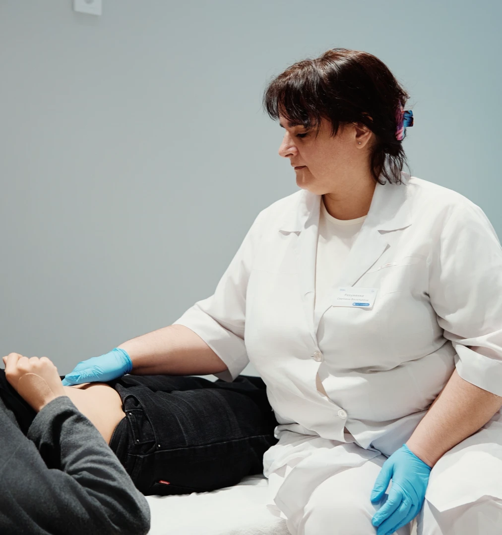 Женщина гинеколог в белом халате осматривает оголенный живот пациентки, лежащей на кушетке.