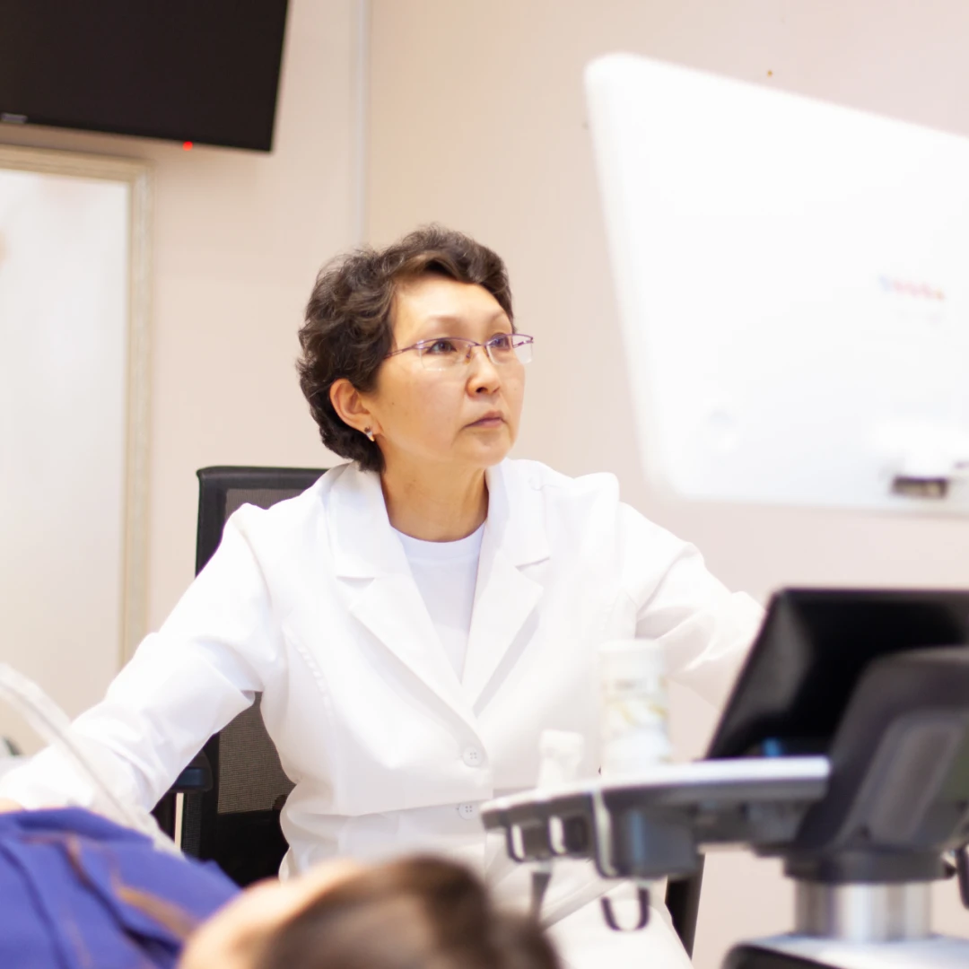 На фото виден живот пациентки крупным планом и рука врача с датчиком УЗИ, проводящего УЗИ сосудов печени.