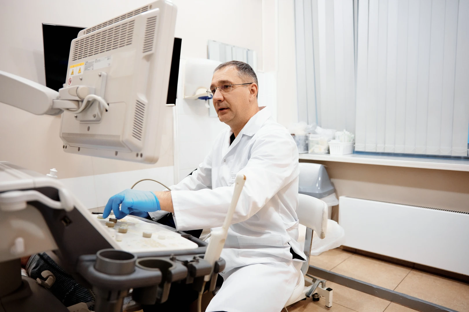 Женщина врач в белом халате рассказывает, что показала эластометрия печени.