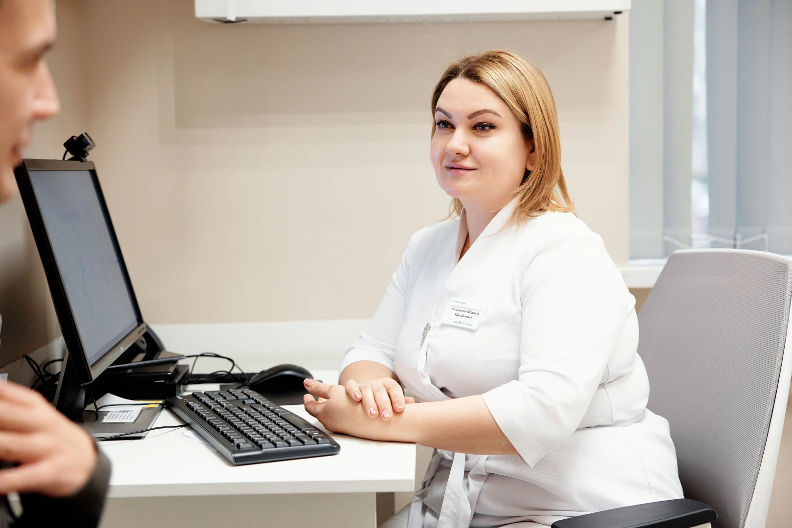 Врач-ортопед в белом халате за рабочим столом разговаривает с пациентом в кабинете