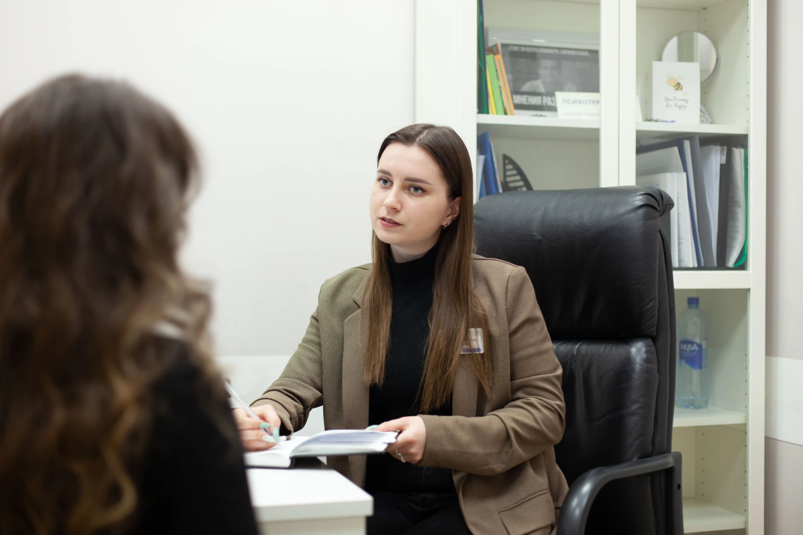 Специалистка и пациентка разбирают записи в открытом блокноте на столе кабинета