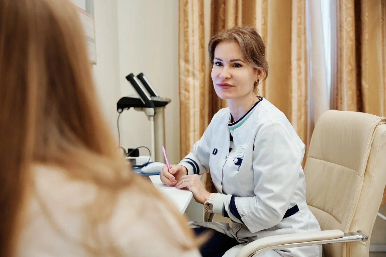 Врач делает записи во время разговора с пациенткой на приёме